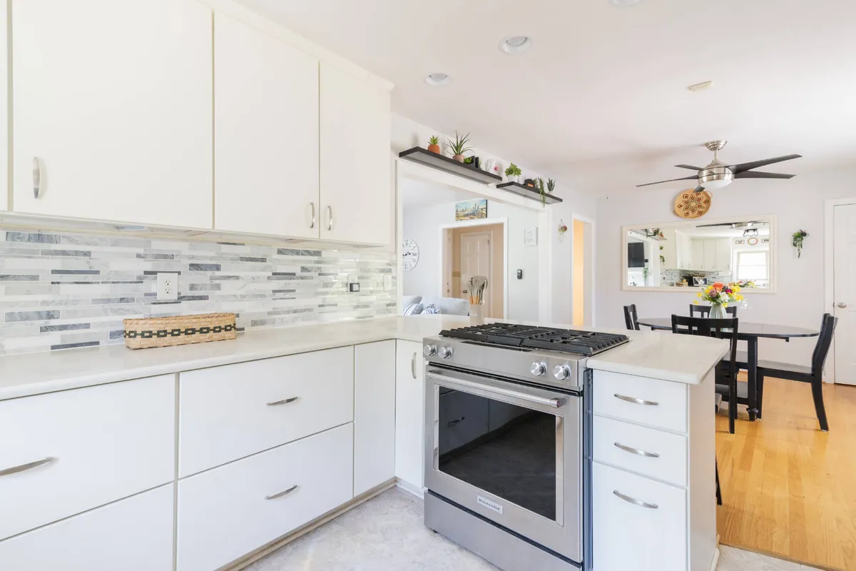 A warm, welcoming kitchen and dining area, with a stainless steel stove, a modern backsplash, and a wooden dining table adorned with flowers. The space blurs the line between cooking and dining, emphasizing togetherness.