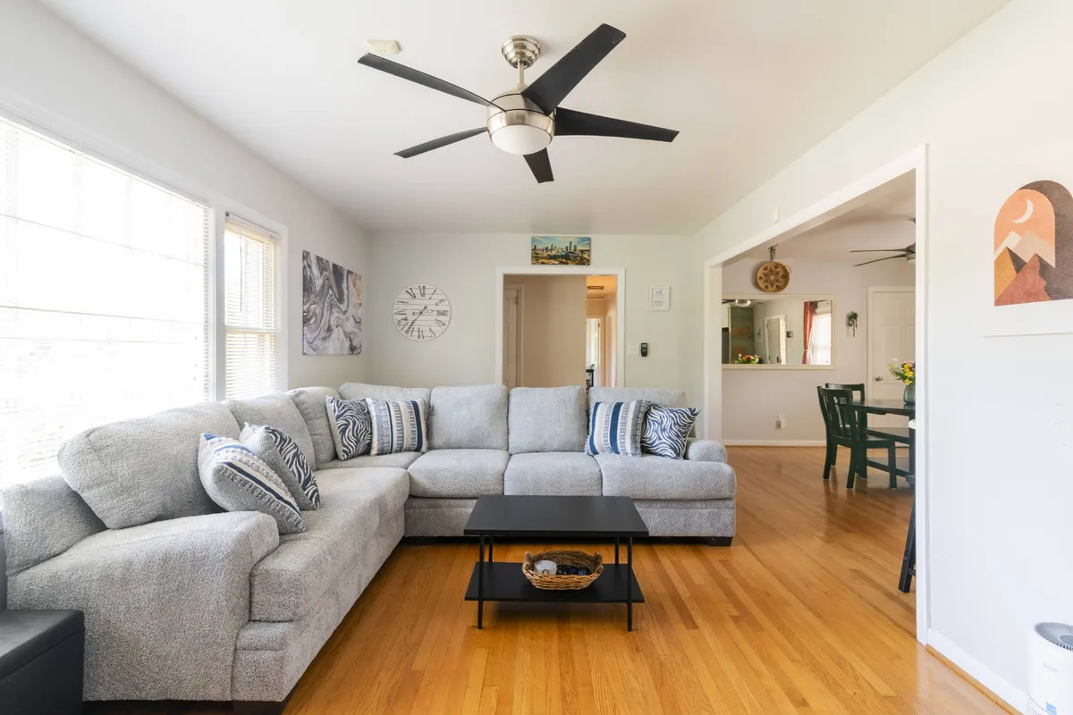 A spacious living room featuring a large plush sectional sofa, a central coffee table, decorative wall art, and a ceiling fan. The arrangement invites relaxation and social gatherings, with ample space for families or friends to enjoy movie nights or conversations.
