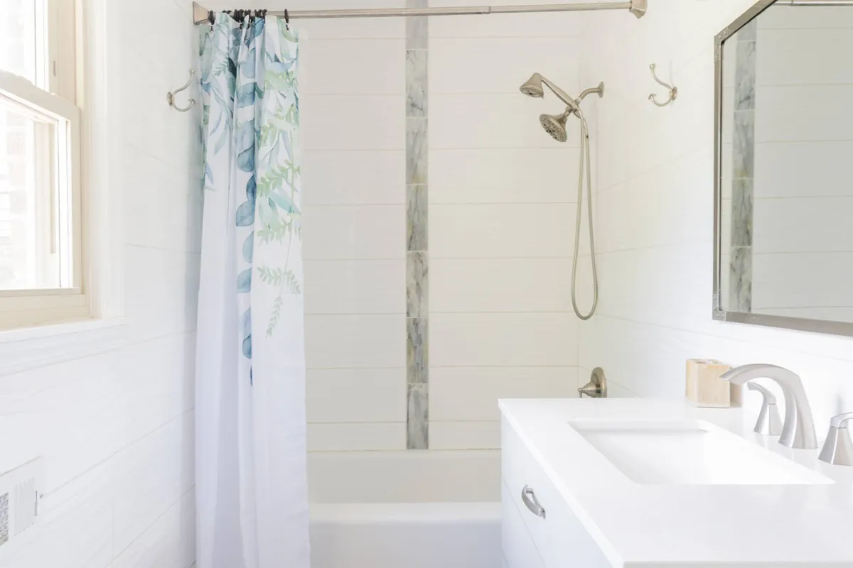 A renovated bathroom featuring a bathtub, modern showerhead, vanity with mirror, and a soft curtain. The space feels calming and fresh, offering a spa-like environment for self-care and relaxation after a long day.