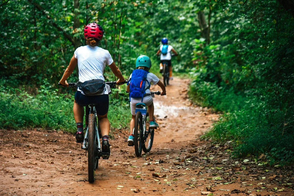 An action-filled outdoor shot with cyclists navigating a dirt path surrounded by trees. The image suggests adventure, recreation, and exploration, highlighting local opportunities for active pursuits and family outings.