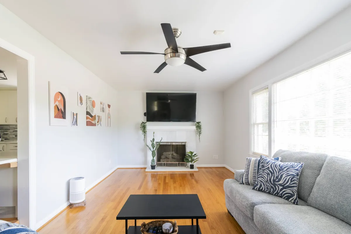 The image showcases a cozy, inviting living room with a plush sofa, stylish coffee table, mounted television above a crackling fireplace, and tasteful wall art. The space feels warm and perfect for relaxation or gathering with friends and family.
