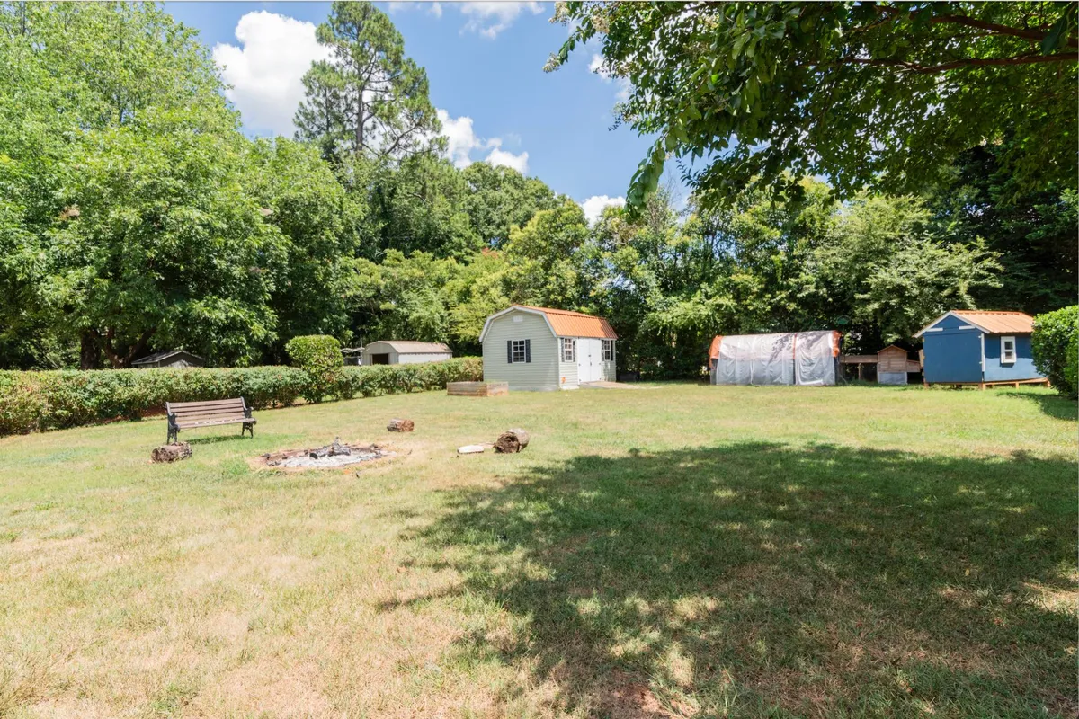 This image showcases a cozy backyard fire pit area surrounded by lush greenery and a small blue shed in the background. The open space is perfect for gatherings and enjoying outdoor activities, with plenty of room for pets and children to play safely within sight.